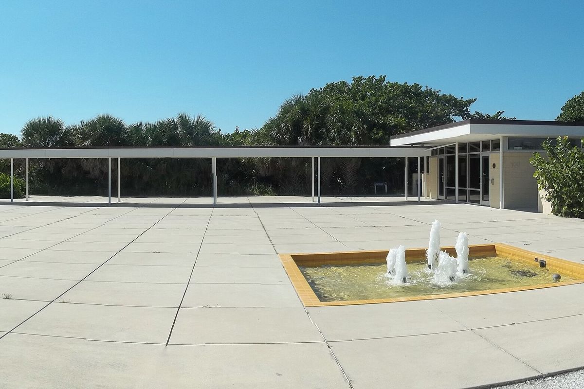 The low, flat-roofed Nokomis Beach pavilion with covered walkways, palms and a fountain on the plaza